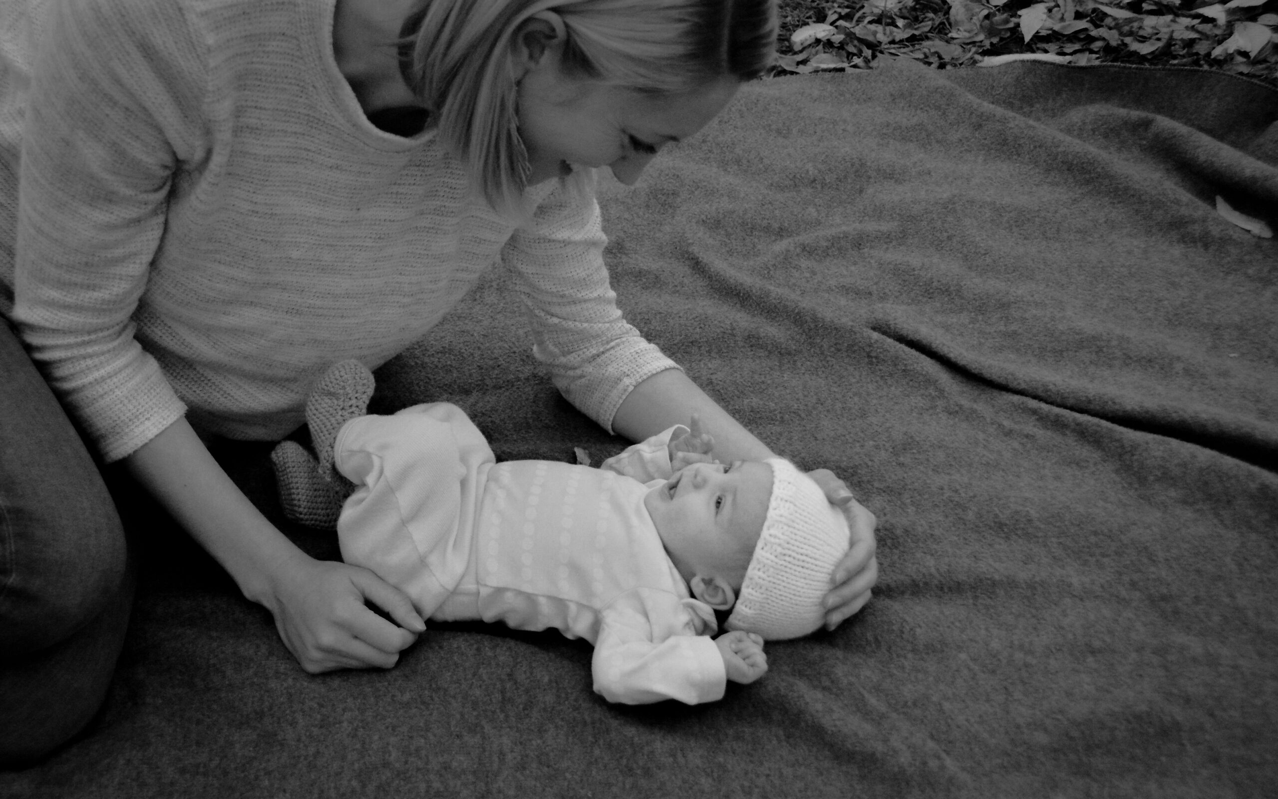 Coach Nina leaning over her two-month-old daughter laying on blanket, black and white