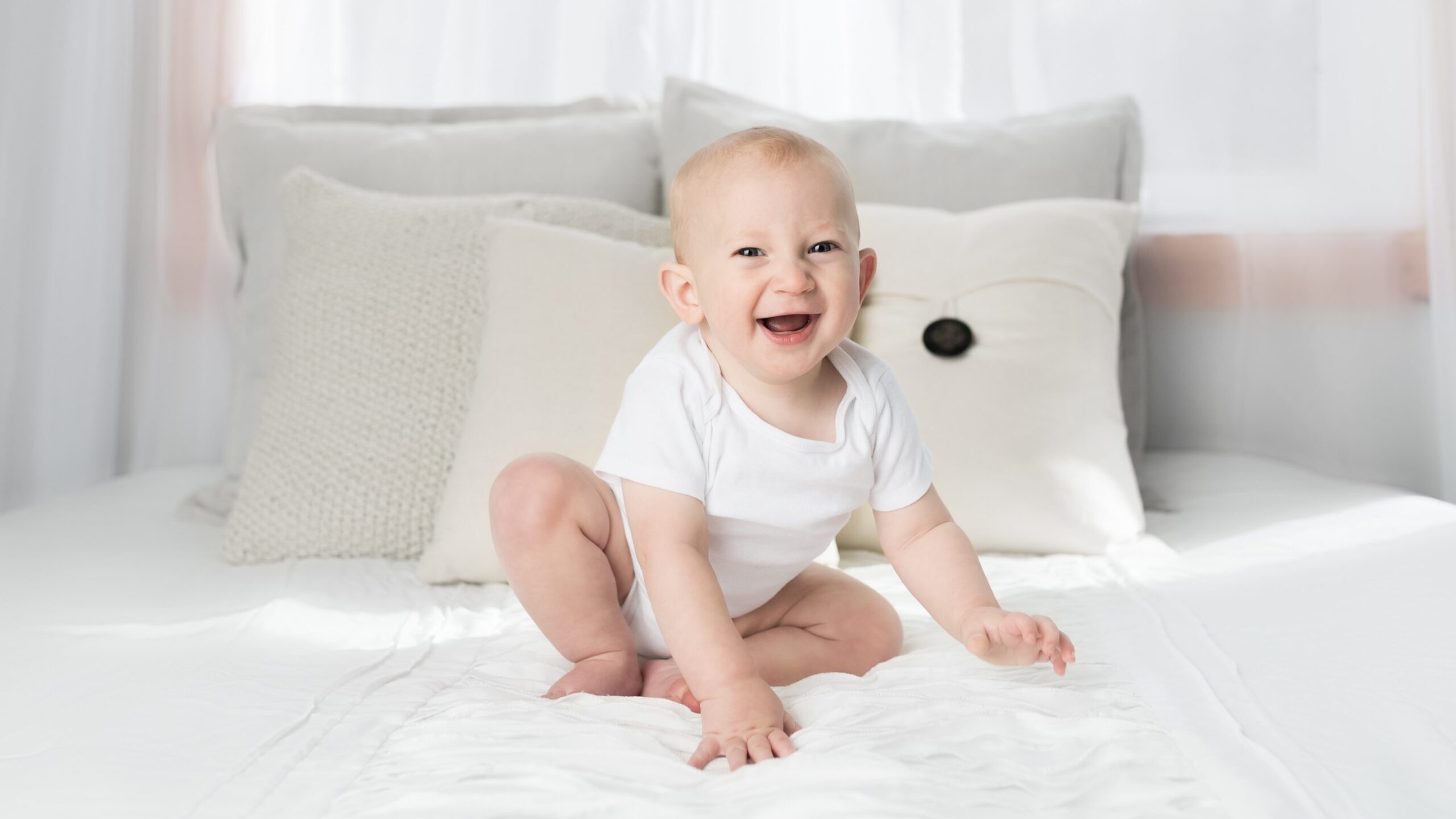 baby sitting and smiling on bed